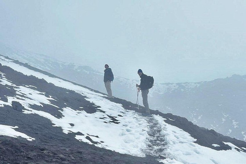 Two hikers on a snowy mountain trail with snow patches and distant mountains. 5