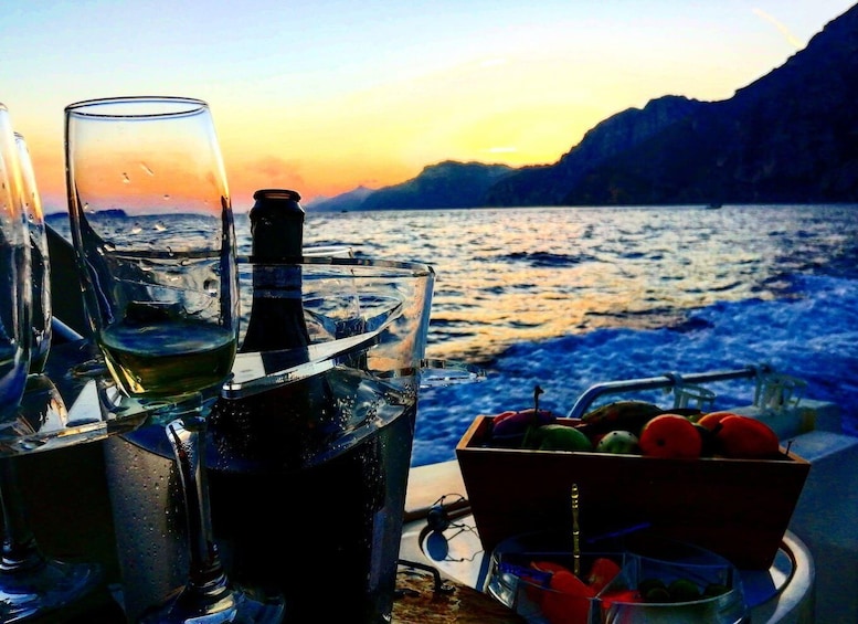 A boat with glasses, a bottle, and a fruit bowl on deck during sunset. 3