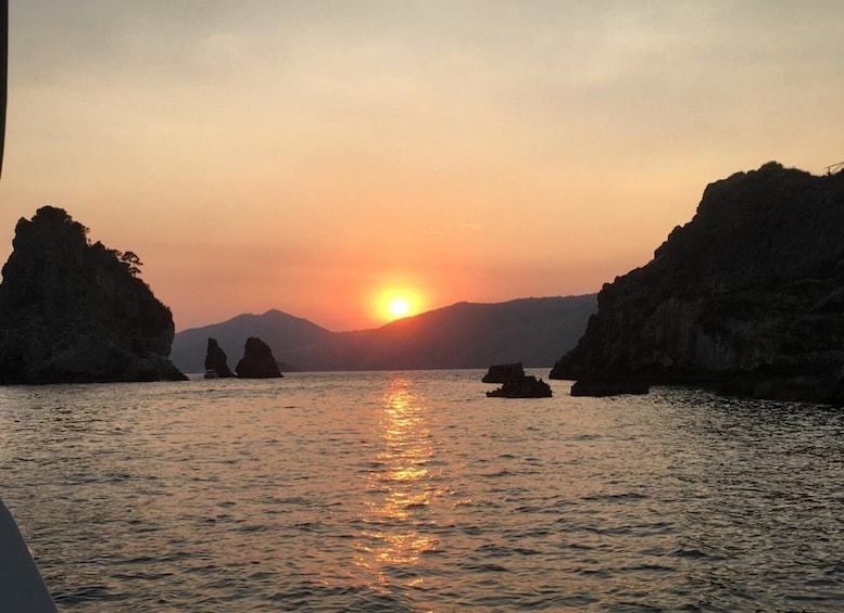 A sunset over a calm sea with rocky outcrops and distant mountains. 2