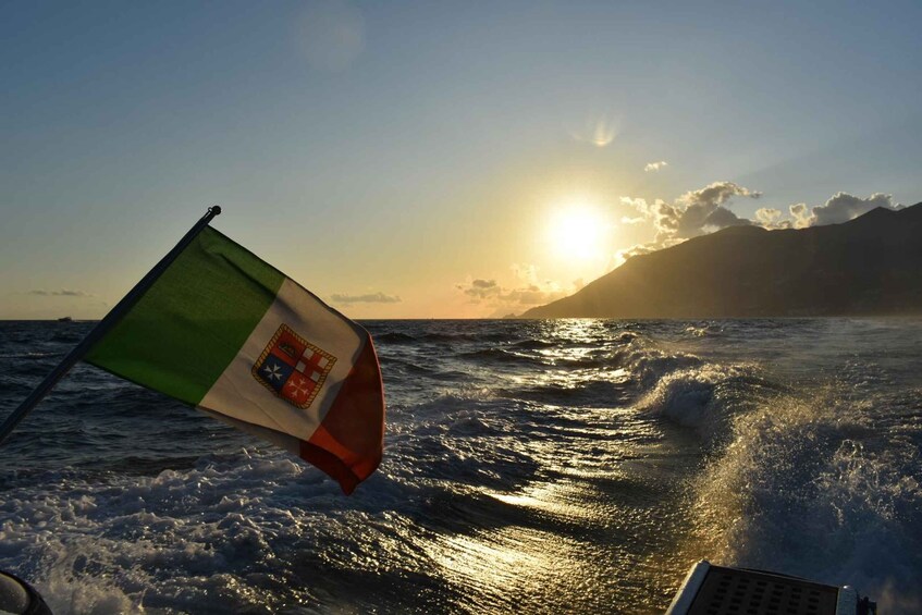 A flag on a boat with a sunset and ocean waves in the background. 1
