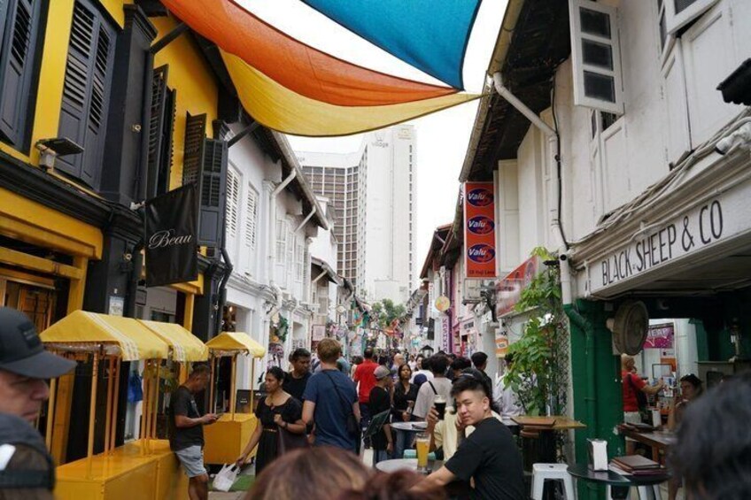 A bustling street with yellow awnings, a Black Sheep & Co shop, and a crowd of people. 5