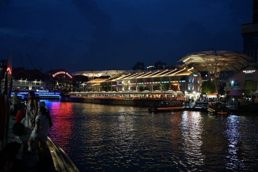 A riverside view at night with illuminated buildings and a boat docked by the riverbank. 4