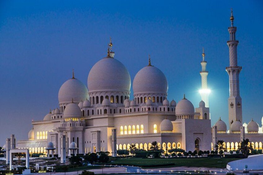 A large, illuminated mosque with multiple domes and minarets, surrounded by well-maintained gardens. 2