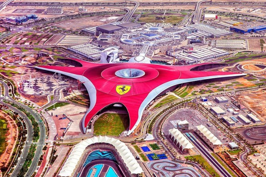 A large, uniquely shaped stadium with a prominent red roof and a Ferrari logo, surrounded by roads and industrial buildings. 5