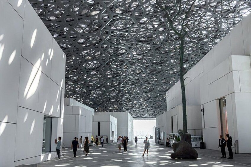 A modern architectural space with a patterned ceiling, large white walls, and a central sculpture. 2