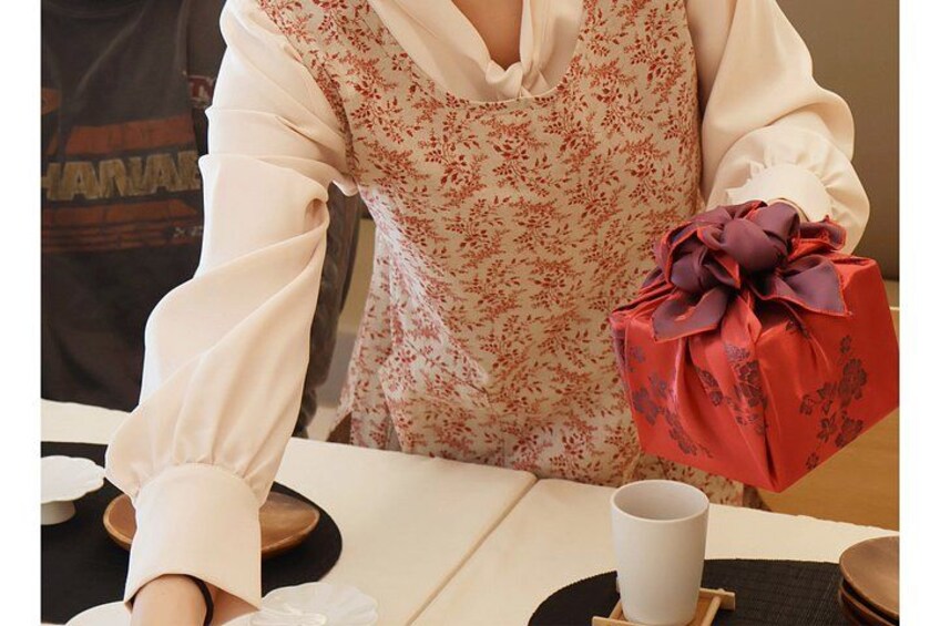 A person holding a red gift box with a bow, wearing a floral dress, and a white shirt. 2
