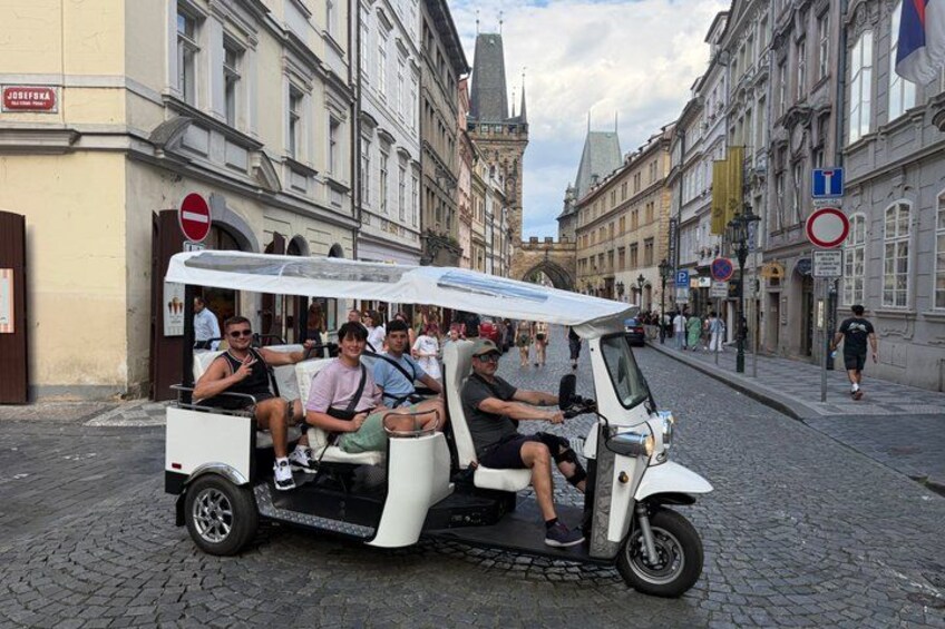 A white electric vehicle with passengers on a cobblestone street in a European city. 2