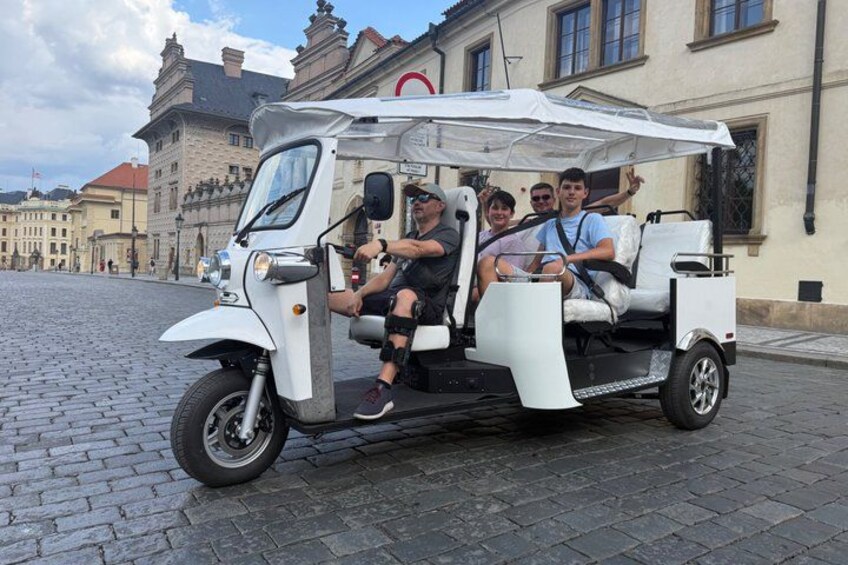 A white three-wheeled vehicle with passengers, parked on a cobblestone street. 5