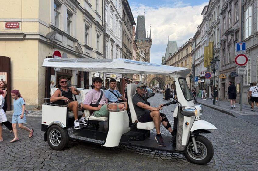 A white electric vehicle with passengers on a cobblestone street. 4