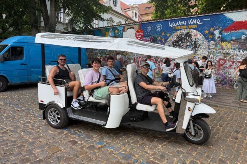 A white electric golf cart with passengers, parked on cobblestone pavement, with a mural in the background. 3