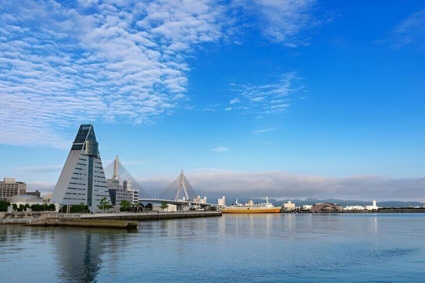 A coastal cityscape with modern architecture, including a prominent pyramid-shaped building and a bridge. 4