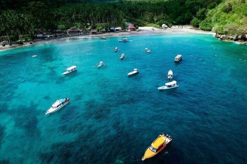 A turquoise sea with several boats, a sandy beach, and a forested area in the background. 4