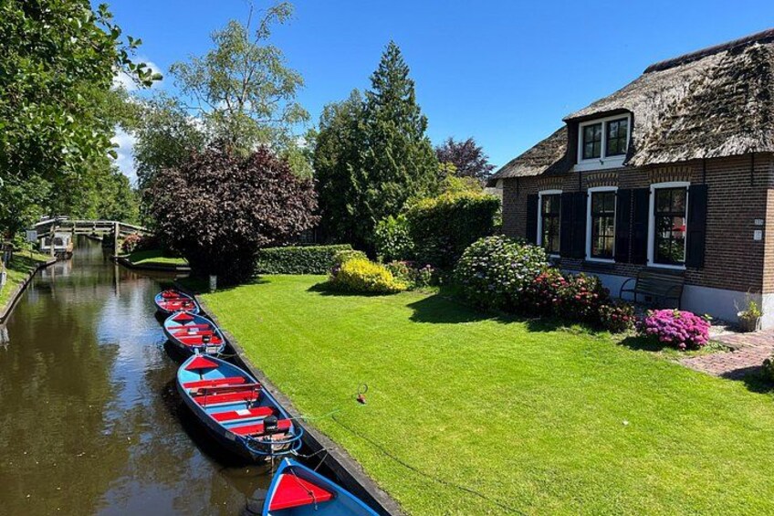 A canal with boats, a grassy area, a house with a thatched roof, and a bridge. 4