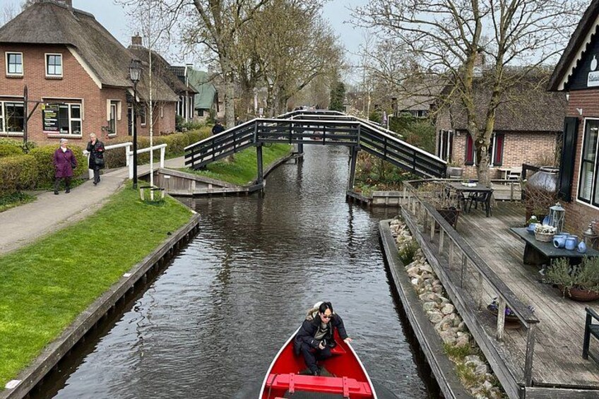 A narrow canal with a red boat, a wooden bridge, and houses along the banks. 5