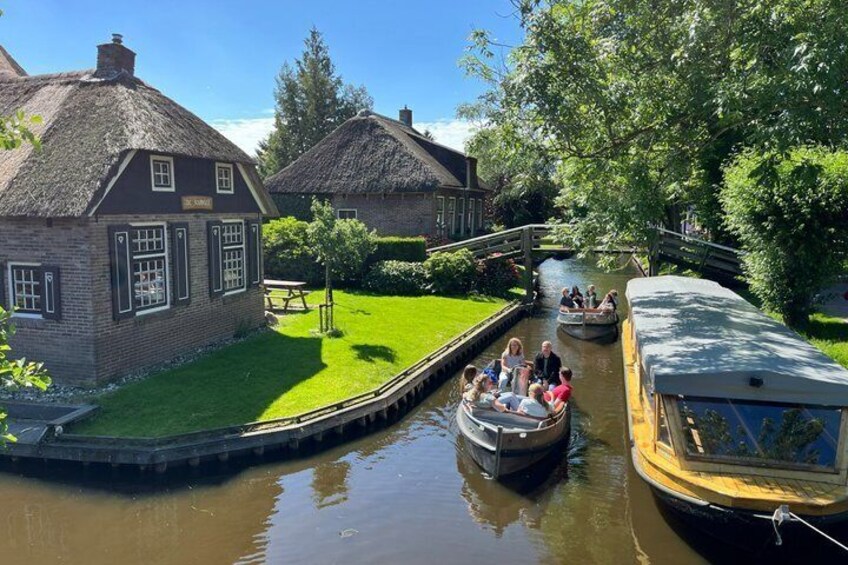 A narrow canal with boats, thatched-roof buildings, and a bridge. 1