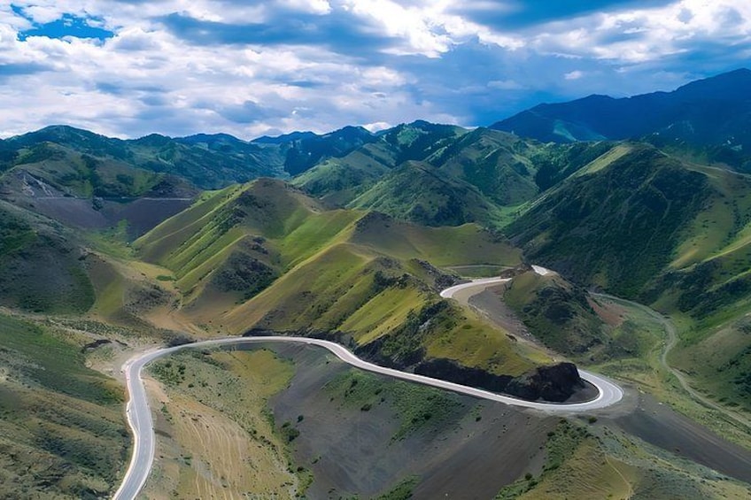A winding road through a mountainous landscape with green hills and a river. 5