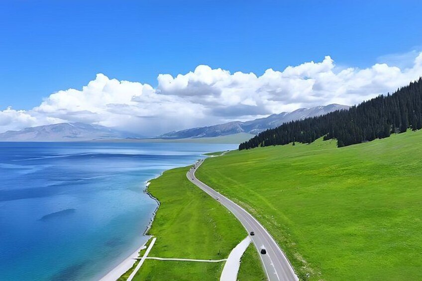 A coastal road with a grassy landscape, a body of water, and mountains in the background. 3