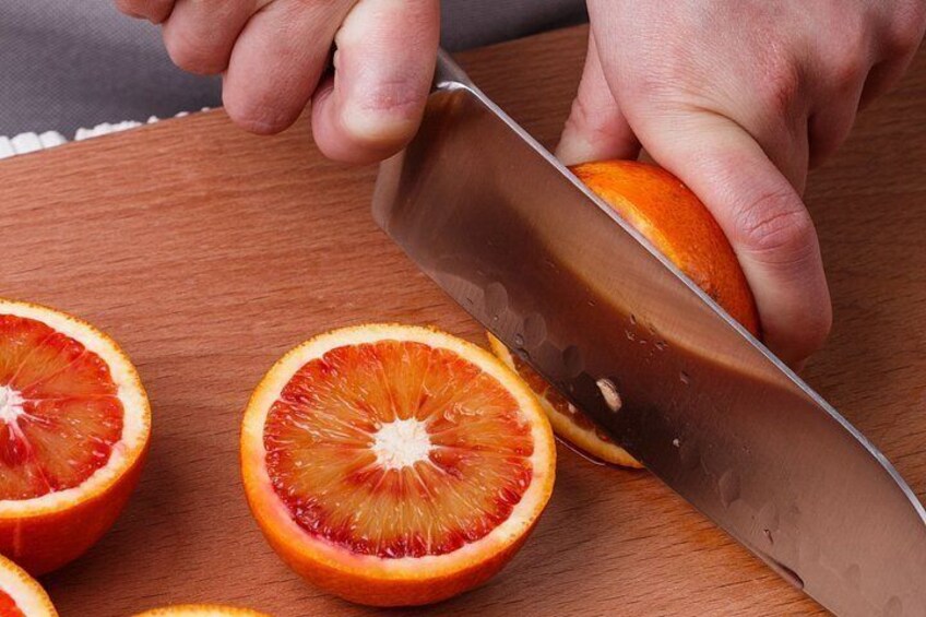 A person cutting a blood orange on a wooden cutting board. 5
