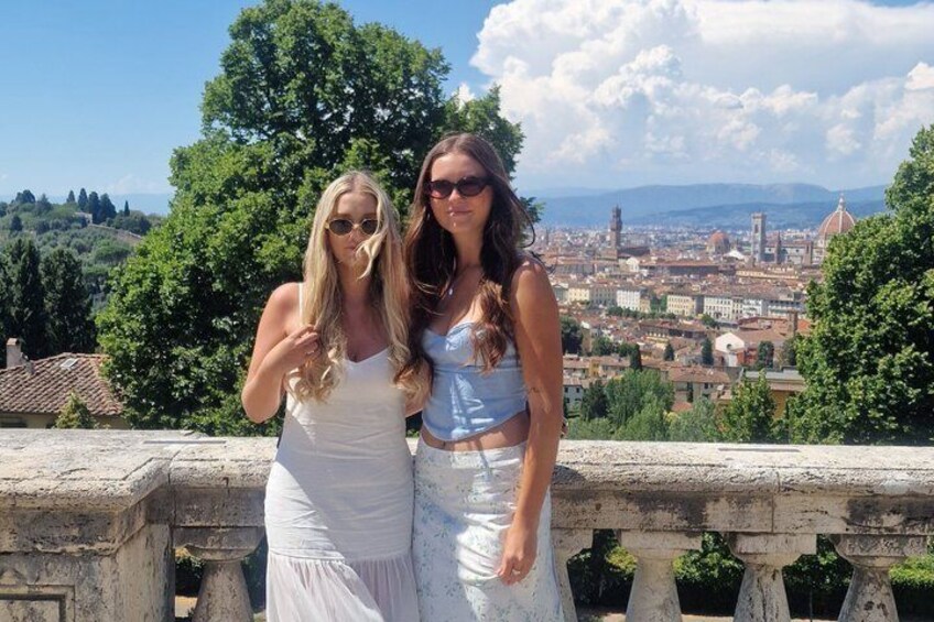 Two women standing on a stone balustrade overlooking a cityscape with historical architecture and greenery. 5