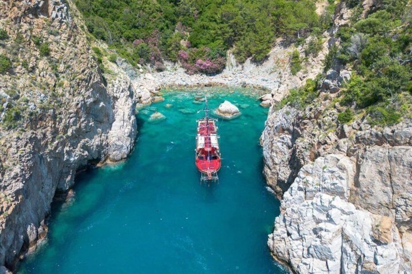 A red boat anchored in a turquoise bay surrounded by rocky cliffs. 1