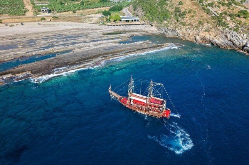 A red fishing boat in the ocean with a rocky coastline and a building in the background. 5