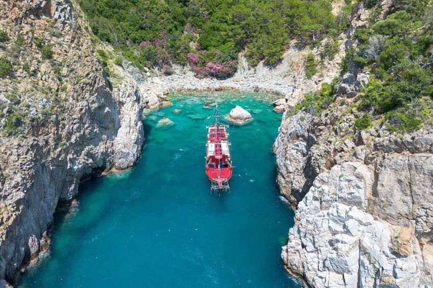 A red boat anchored in a narrow, rocky waterway surrounded by cliffs. 1