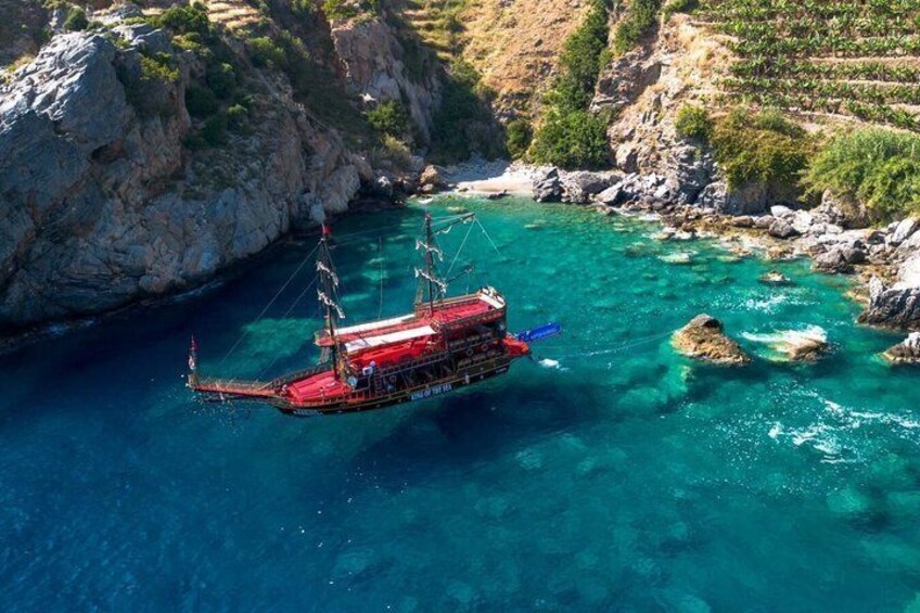 A red boat anchored in clear turquoise waters surrounded by rocky cliffs. 4