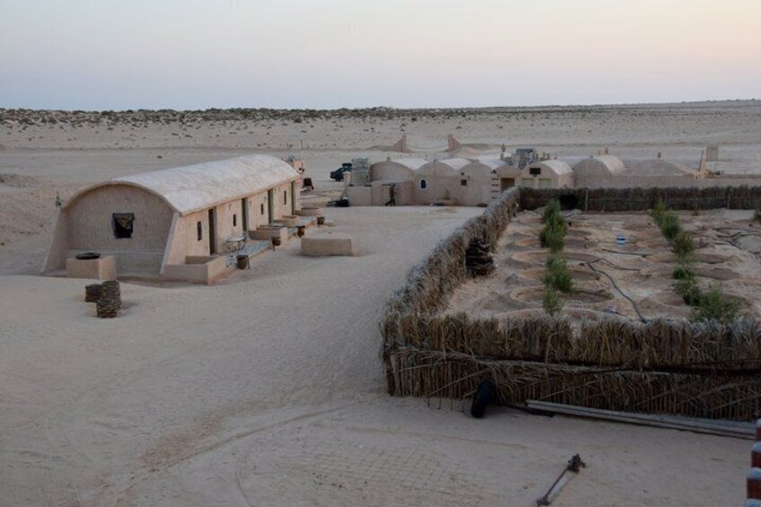 A desert landscape with traditional mud-brick dwellings, a clear sky, and sparse vegetation. 4