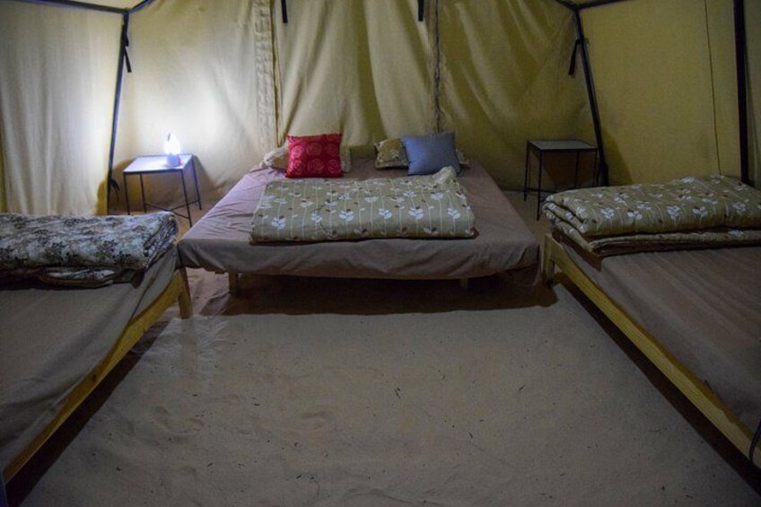 A tent with two beds, each with a pillow and a blanket. There is a small table with a light on it. 4