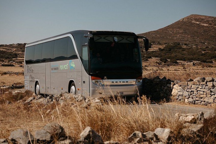 A bus parked in a rocky, grassy area with a stone wall and a hill in the background. 2