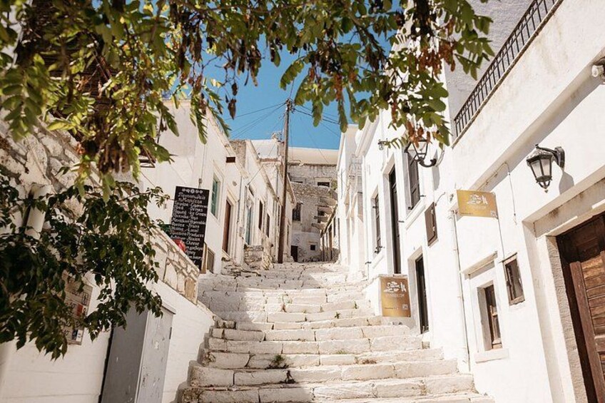 A narrow street with stone steps leading up to a building entrance, surrounded by white walls and a tree. 3