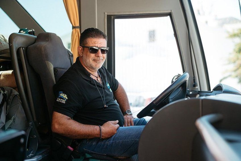 A man sitting in a vehicle with a steering wheel, wearing a black polo shirt and sunglasses. 2