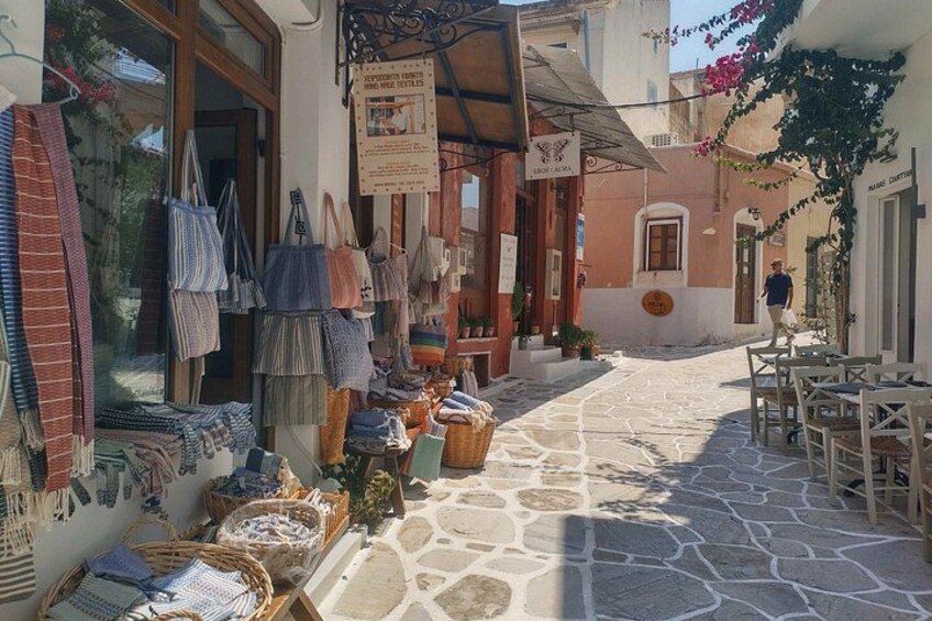 A narrow street with shops, outdoor seating, and stone pavement. 2