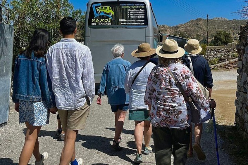 A group of people walking towards a bus labeled 'MAXOS BUS TRANSFER' with contact information and a website. 5