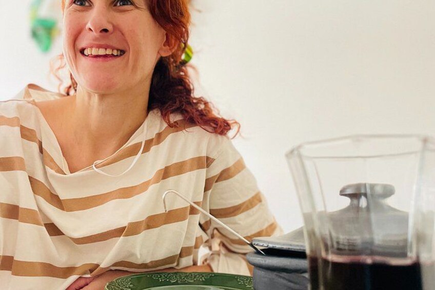 A person wearing a striped shirt, sitting at a table with a glass of dark liquid, possibly wine, and a green plate with a design. 3