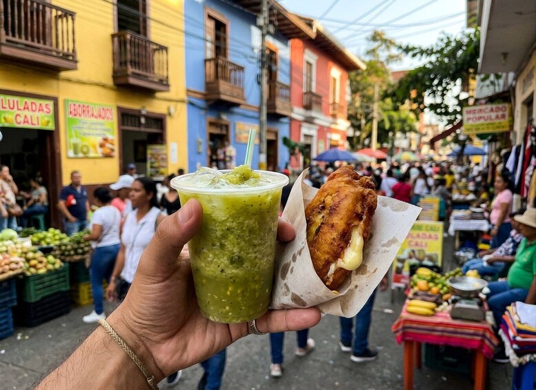 A hand holding a green drink and a fried food item in a market. 1