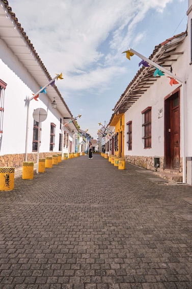 A cobblestone street lined with white and yellow buildings, decorated with colorful paper kites. 3
