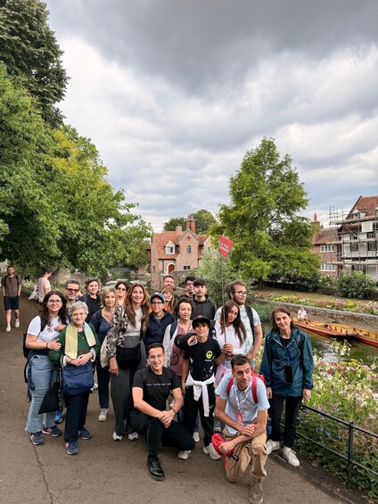 A group of people posing in a park with a river, trees, and historic buildings in the background. 3