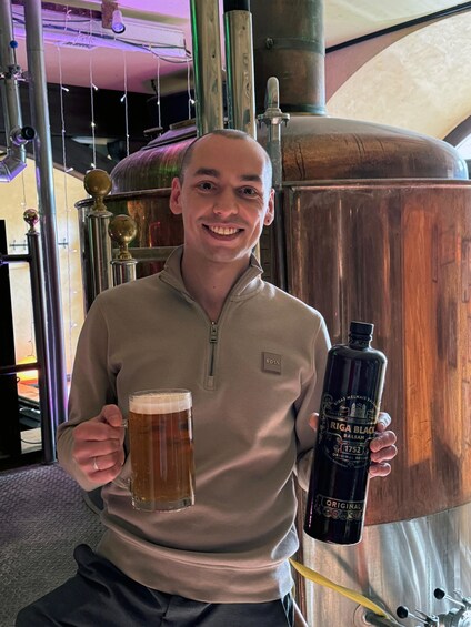 A person holding a beer mug and a bottle of Riga Black Balsam. 2
