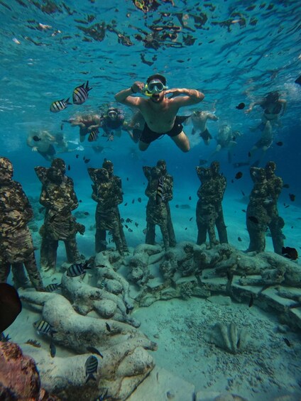 A diver surrounded by marine life and underwater sculptures. 2