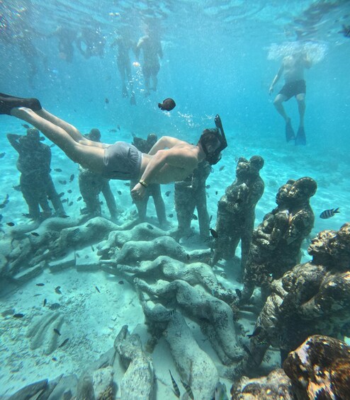 A diver swimming among coral formations with other divers in the background. 4