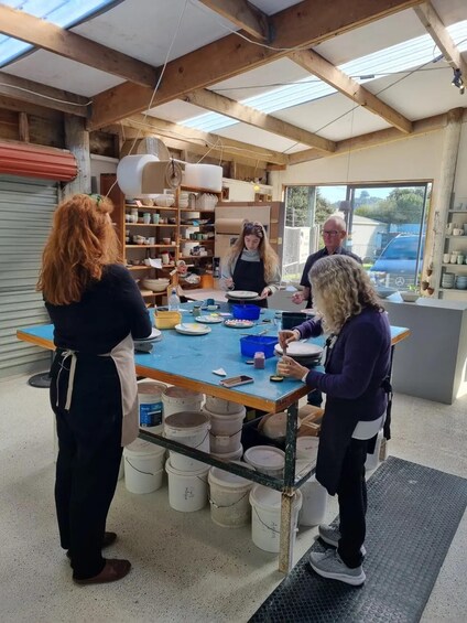 A pottery workshop with people working on pottery wheels and shelves with pottery and tools. 2