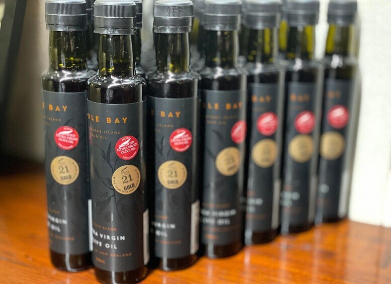 A row of dark bottles labeled 'BLE BAY' with '21 GOLD' and 'EXTRA VIRGIN OLIVE OIL' on a wooden surface. 4