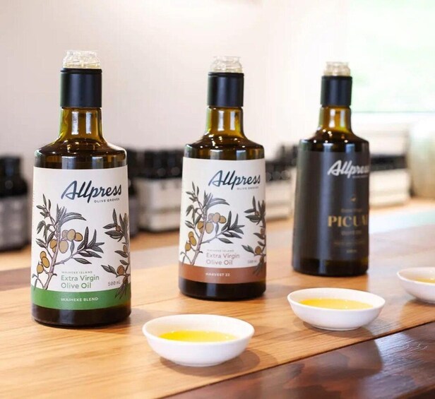 Three bottles of Allpress Extra Virgin Olive Oil on a wooden surface with small bowls containing oil. 3