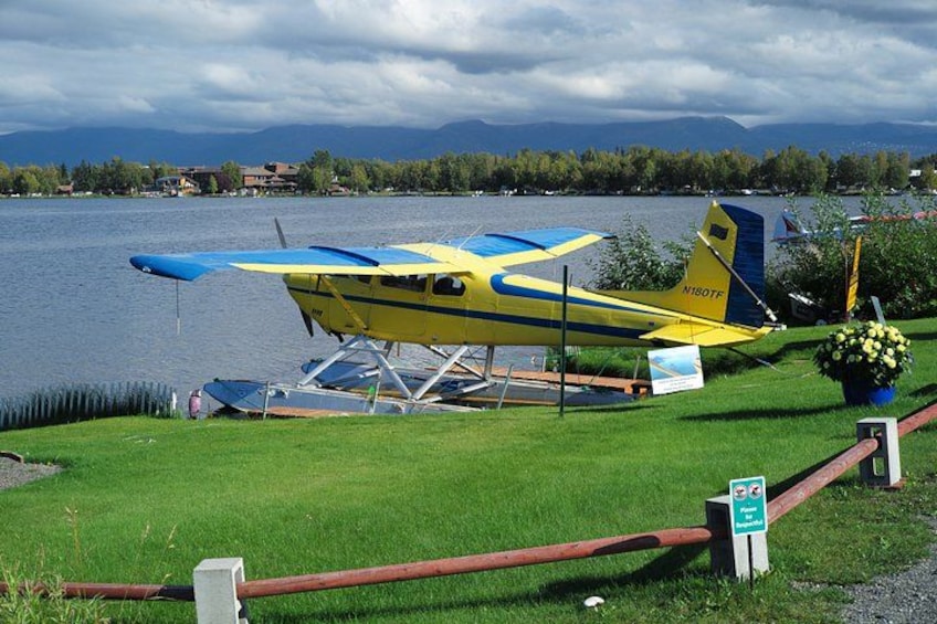 A yellow and blue seaplane parked on a grassy area near a lake. 2