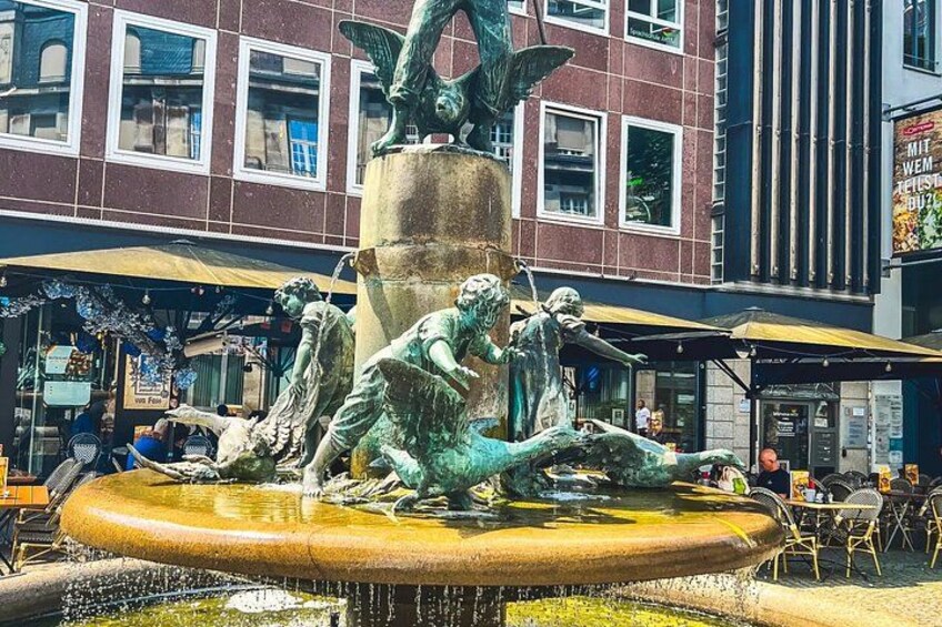 A bronze statue of a man and a woman on a fountain, surrounded by outdoor seating and a building in the background. 4