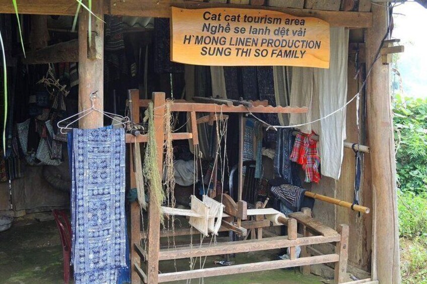 A traditional loom with blue patterned fabric, a sign indicating a tourism area, and a rustic wooden structure. 2