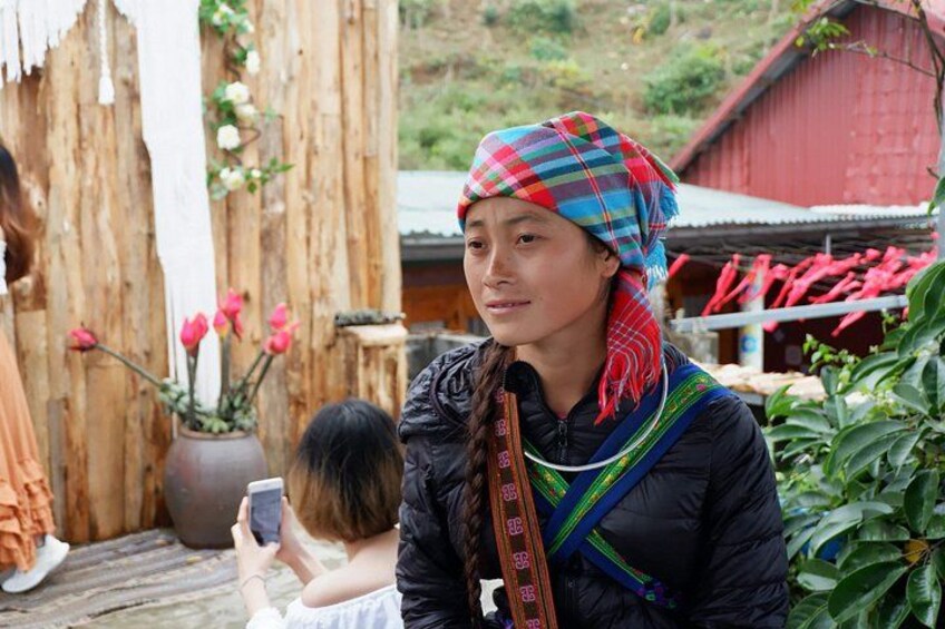 A person in traditional attire with a colorful headscarf, a child, and a rustic wooden structure with flowers in the background. 3