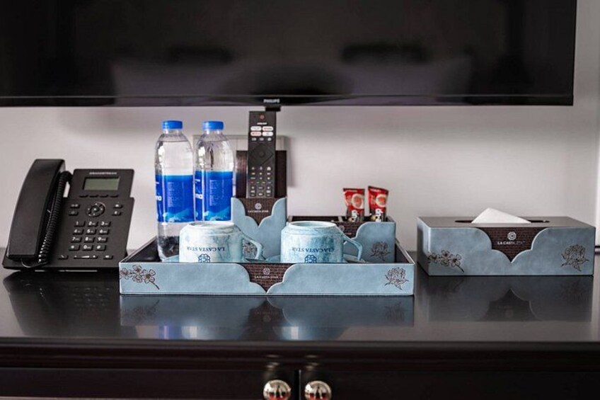 Habitación de hotel con escritorio, teléfono, dos botellas de agua, caja de pañuelos y control remoto. 2