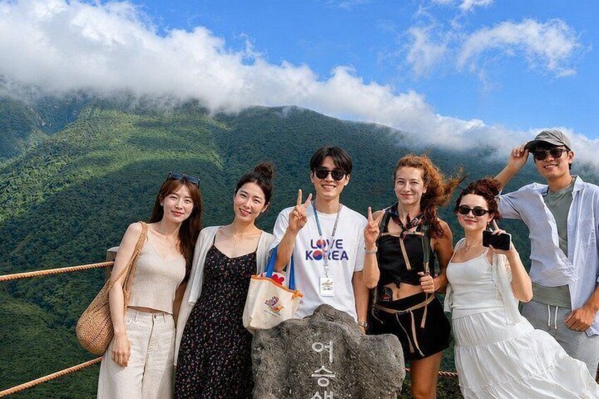 A group of people posing on a mountain ridge with a lush green valley in the background. 1